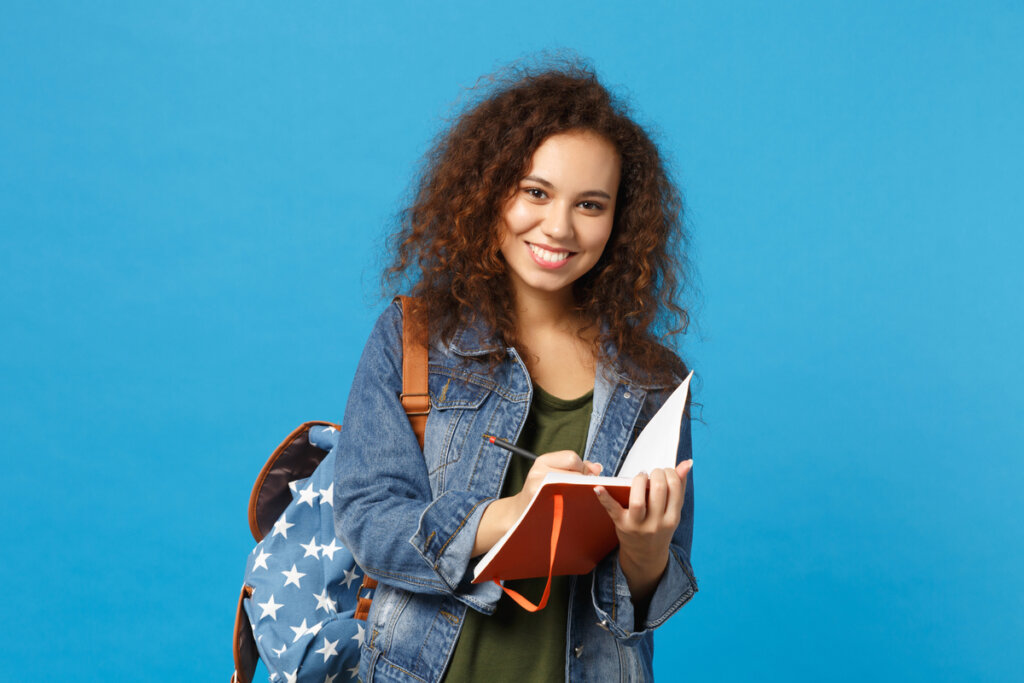Mulher de jaqueta jeans segurando livros e com mochila nas costas