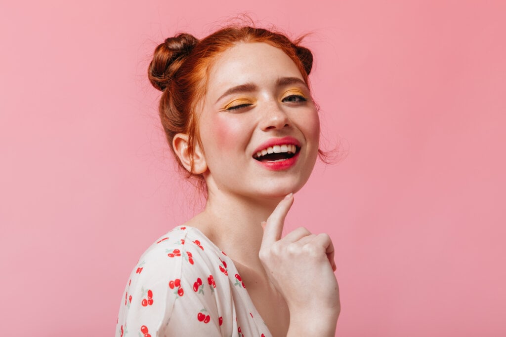 Mulher de maquiagem sorrindo com a mão no queixo