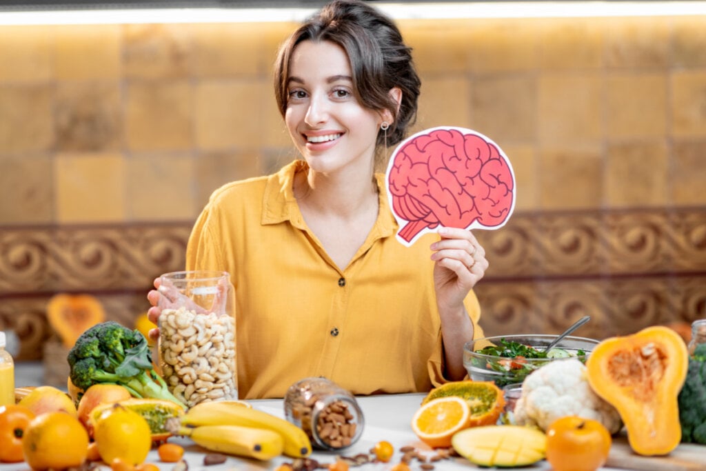 Mulher sorrindo segurando o desenho de um cérebro com uma mesa com alimentos