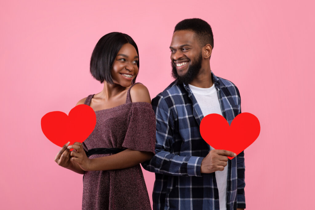 Homem e mulher em frente a um fundo rosa se olhando e segurando corações