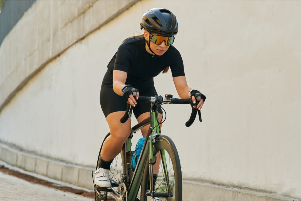 Ciclista com roupa preta, capacete preto e óculos de sol vermelho andando de bicicleta