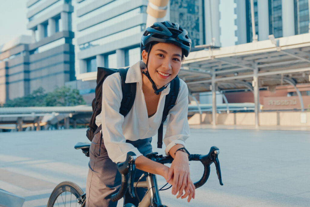 Mulher em cima de uma bicicleta sorrindo com capacete na cabeça e mochila nas costas