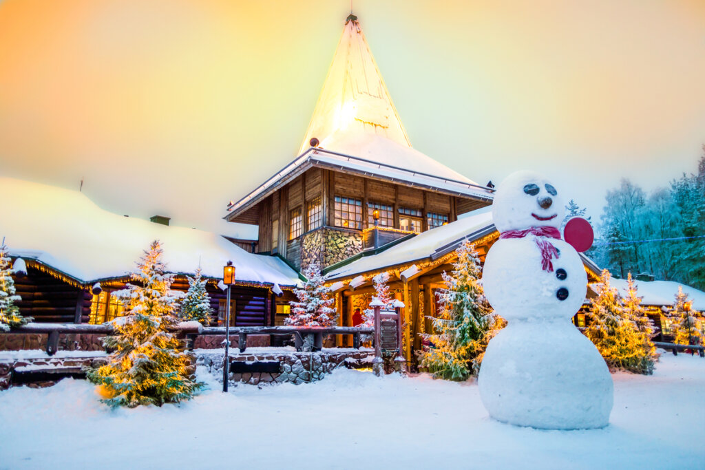 Vista da casa do Papai Noel coberta de neve e um boneco de neve na frente