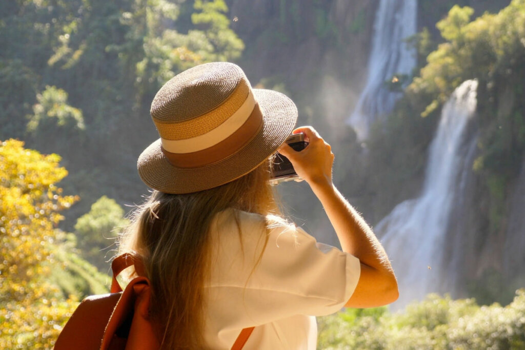 Mulher segurando uma câmera tirando foto de uma cachoeira