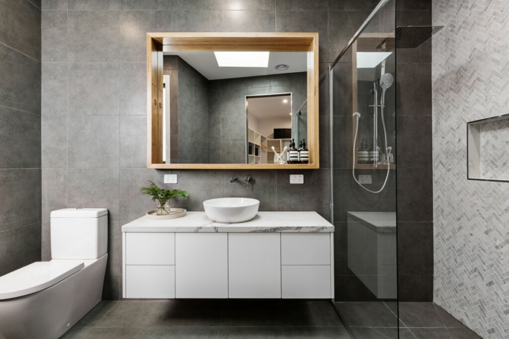 Banheiro com parede cinza, espelho, box e pia branca