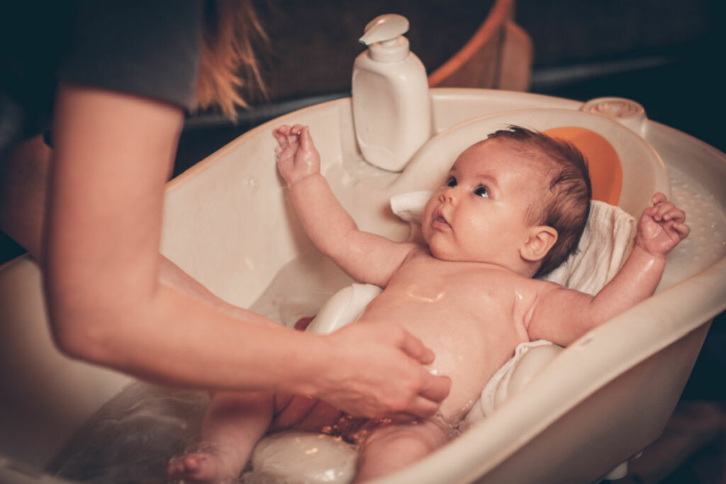 Mulher dando banho em bebê dentro de banheira 