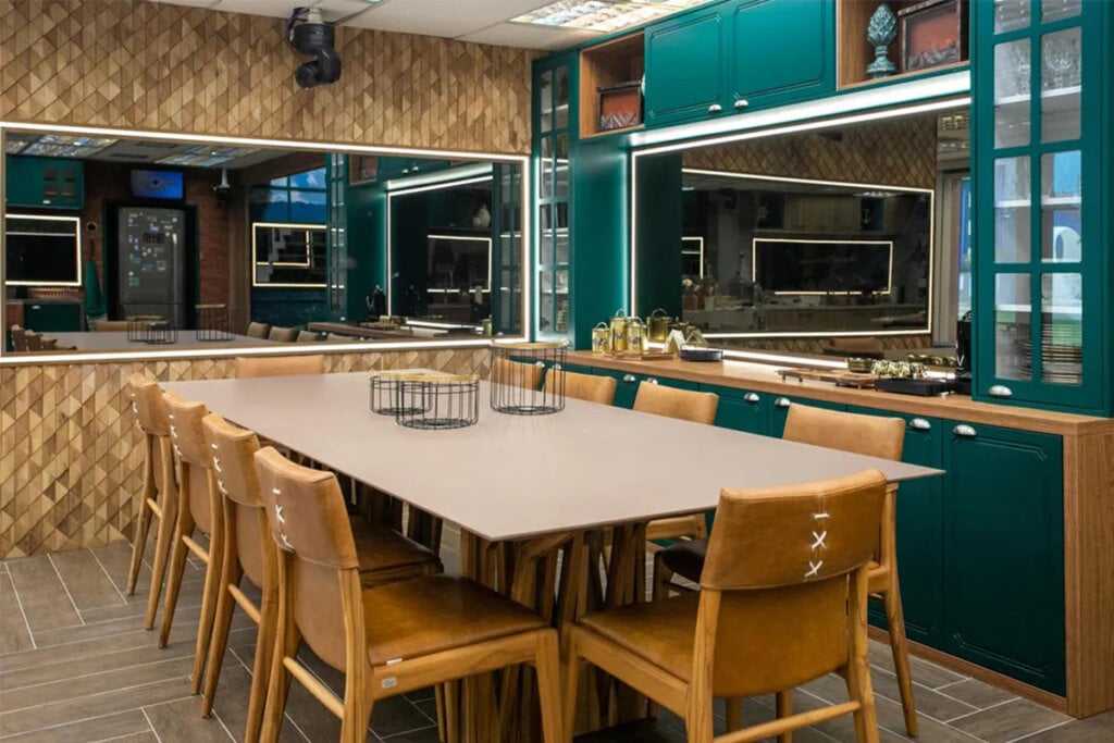 Cozinha VIP do BBB 23 com mesa e cadeiras em tom marrom e armários em verde