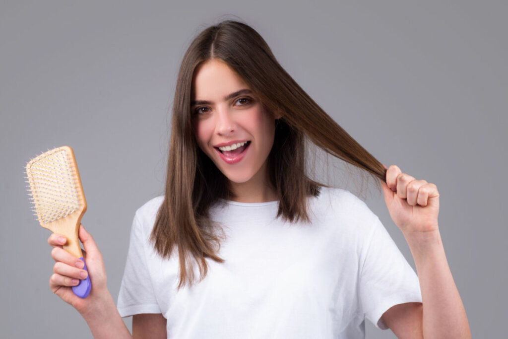 Mulher segurando o cabelo com uma mão e na outra uma escova de cabelos 