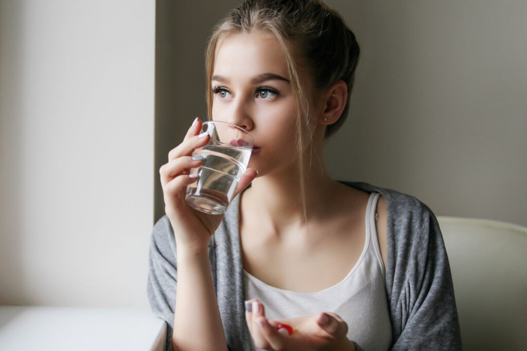 Mulher tomando água em copo de vidro e segurando comprimidos na mão 