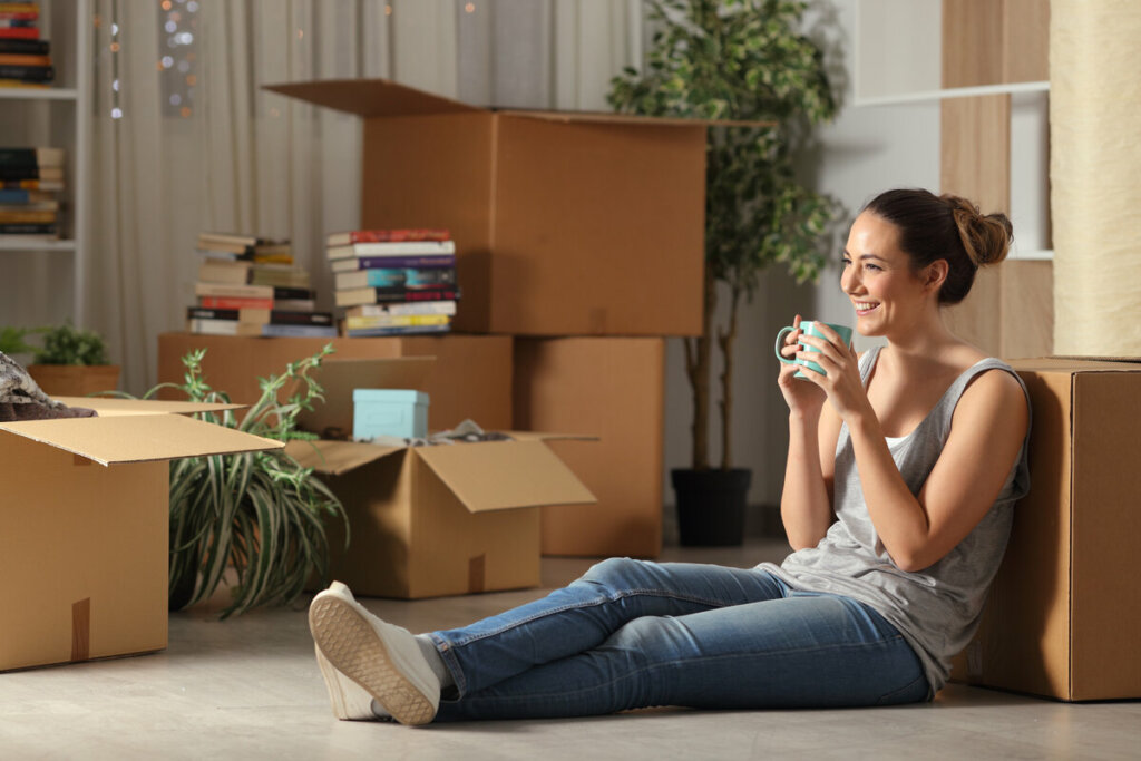 Mulher sentada no chão segurando xícara com caixas em volta