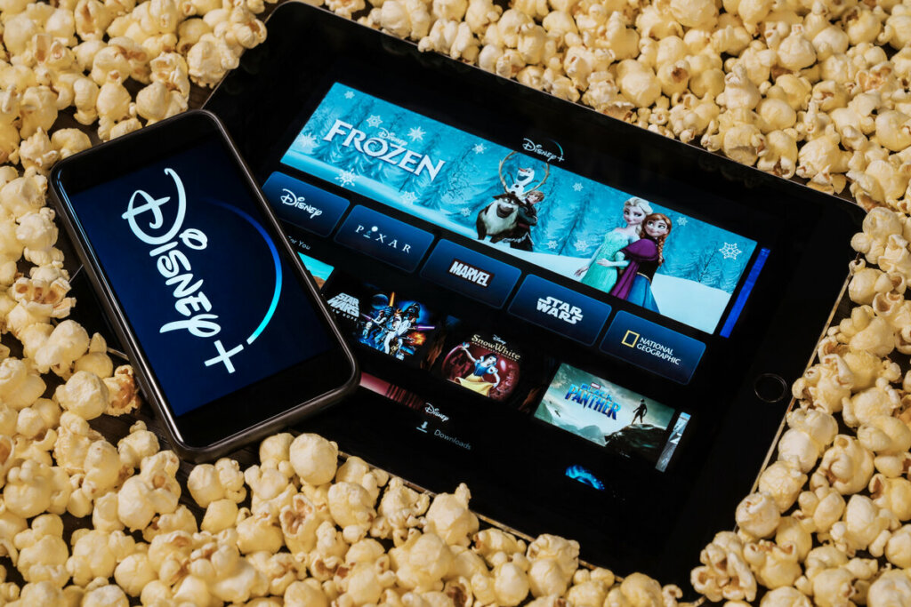 Celular com logo da Disney+ e um tablet no site da plataforma em cima de pipocas