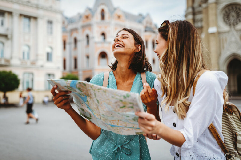 Duas mulheres sorrindo olhando mapa em uma rua