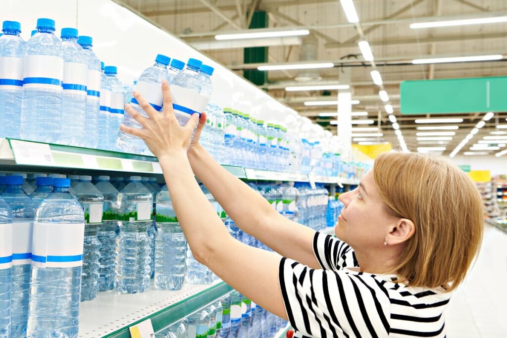 Mulher pegando garrafas de água em prateleira de um supermercado