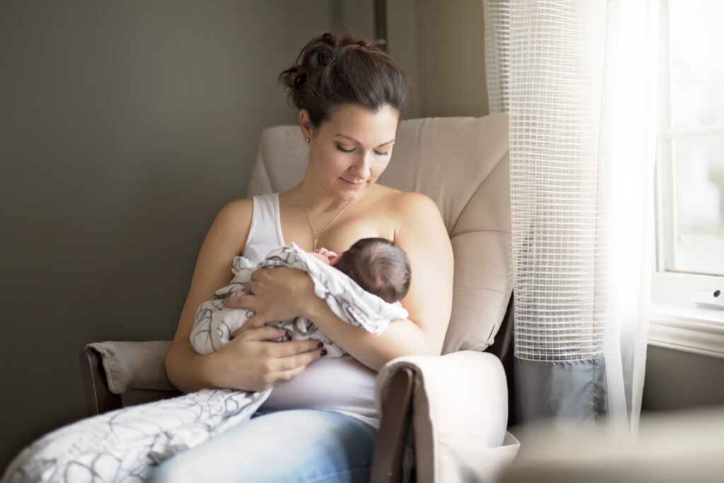 Mulher sentada em uma poltrona amamentando um bebê
