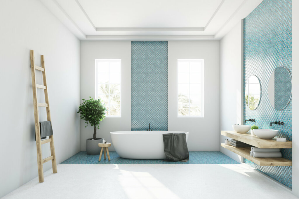 Banheiro com paredes brancas e azuis com banheira, janelas e vaso de planta