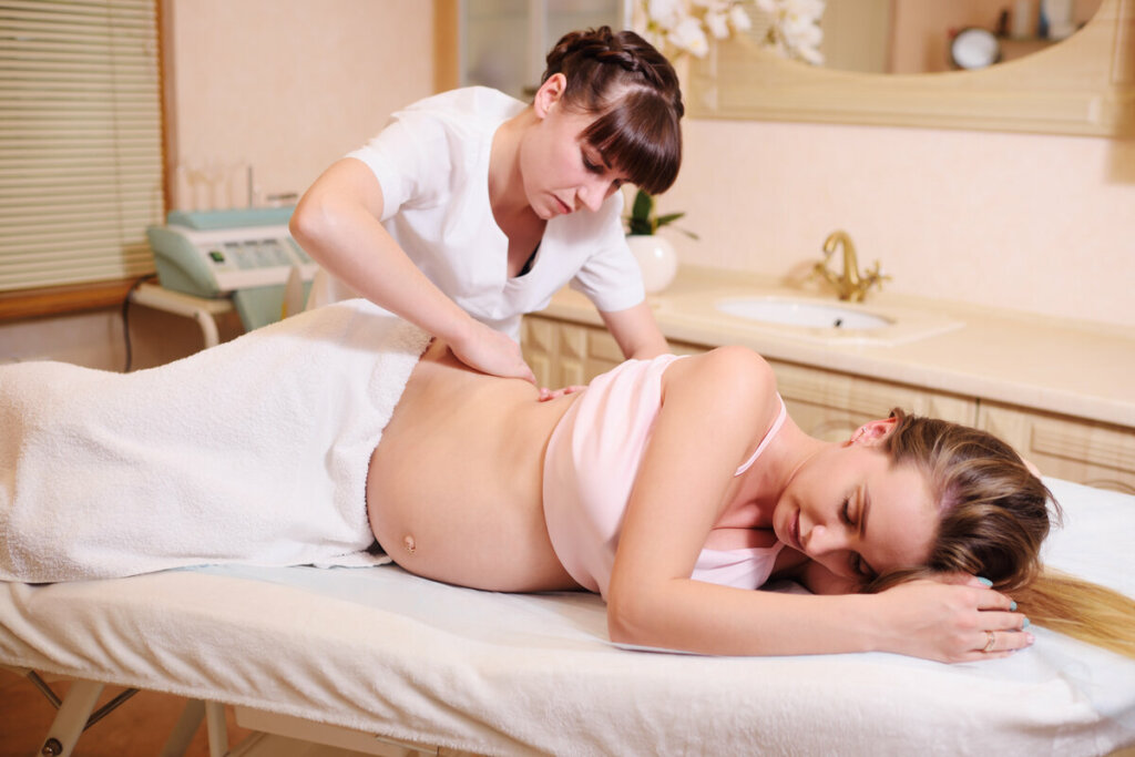Mulher gravida deitada com uma mulher fazendo massagem em sua barriga