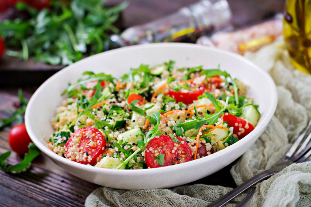 Tabule de quinoa em pote branco com tomate, cenoura, pepino e outros vegetais