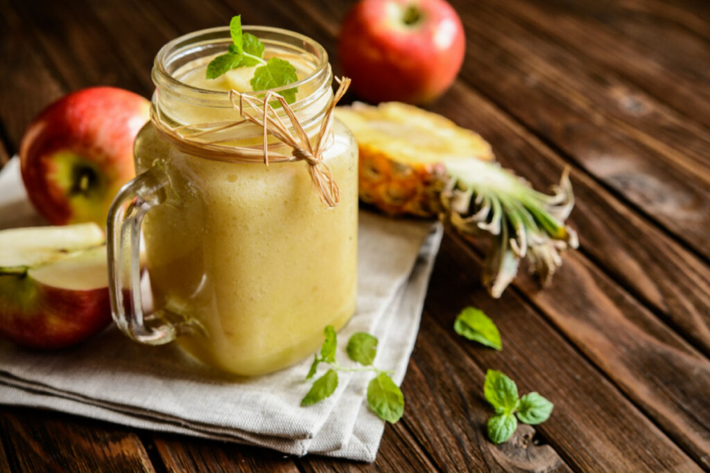 Vitamina amarela em copo de vidro com maçã e abacaxi ao lado
