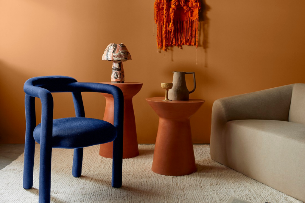 Sala de estar com parede laranja, cadeira azul, mesa de centro laranja e sofá bege 