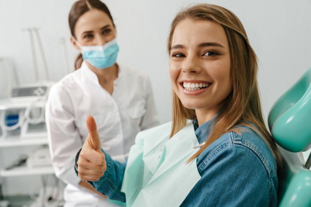 Mulher sorrindo em cadeira de dentista e dentista ao fundo