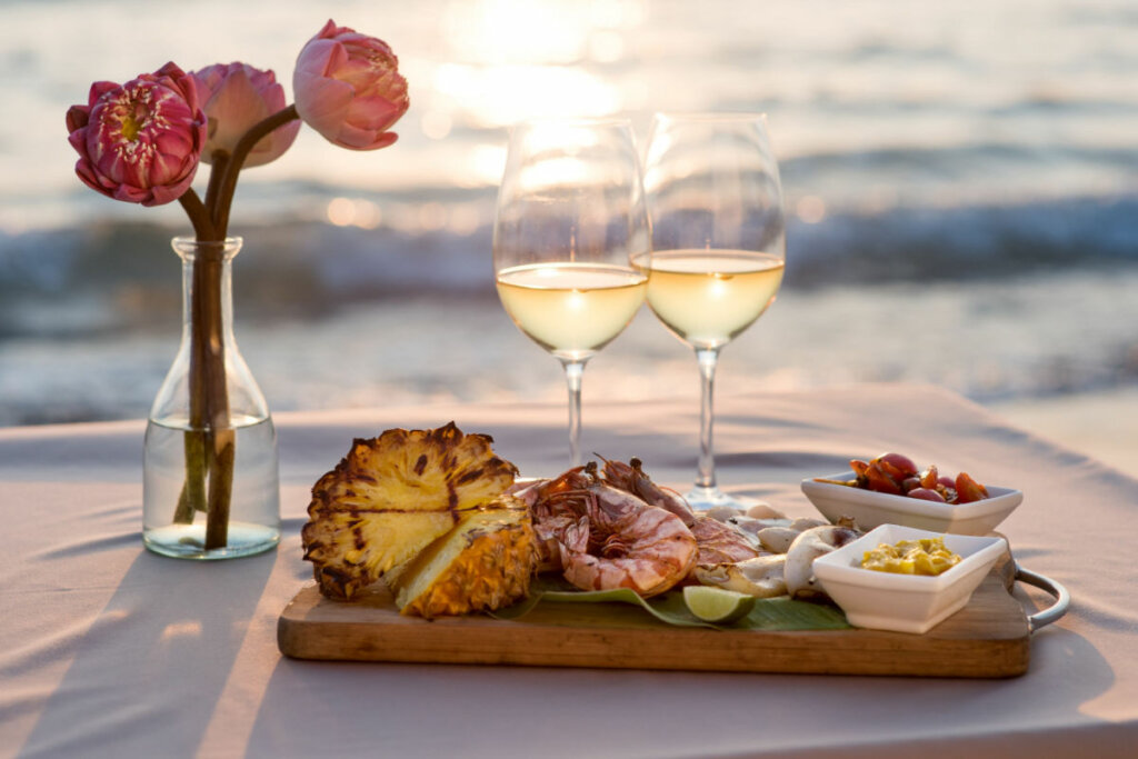 Duas taças com vinho branco em ciima de bandeja com frutas e petiscos de praia