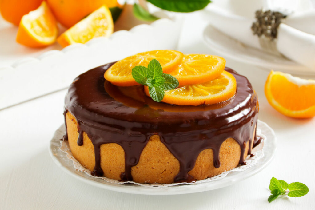 Bolo de laranja com cobertura de chocolate com rodelas de laranja e folhas de hortelã