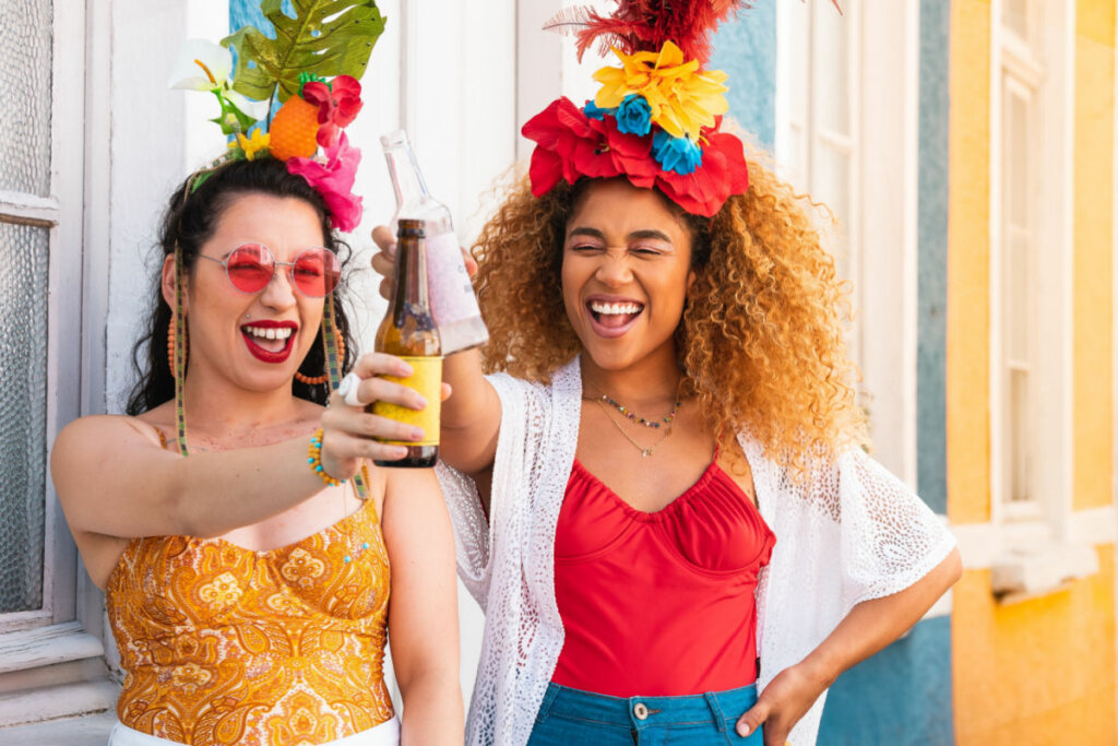 Duas mulheres com roupa de carnaval e brindando com garrafa de bebida