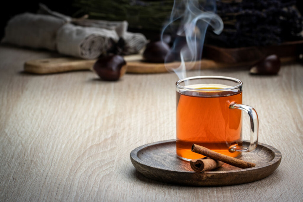 Xícara com chá marrom em cima de pires de madeira e paus de canela ao lado