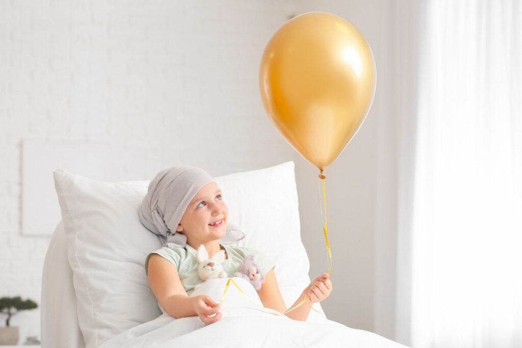 Criança deitada em cama de hospital segurando um balão dourado