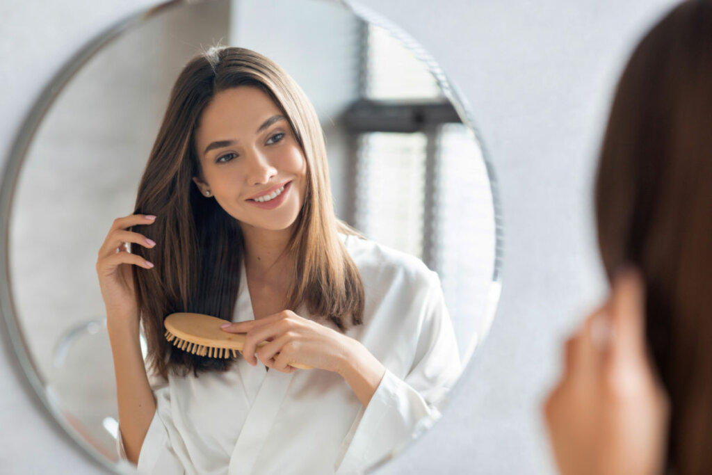 Reflexo no espelho de mulher passando escova no cabelo