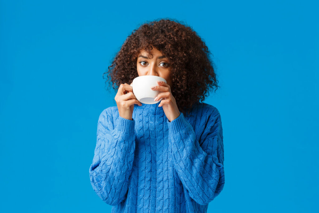 Mulher de blusa azul segurando xícara branca na boca