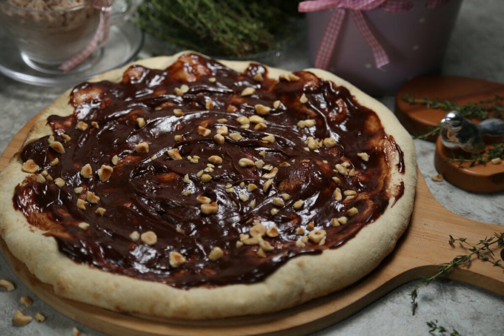 Pizza de chocolate polvilhada com castanha de caju em cima de uma tábua de madeira