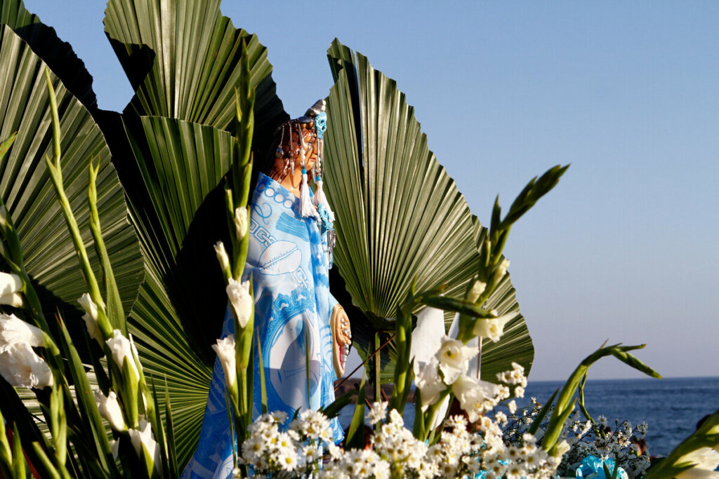 Estátua de Iemanjá rodeada de flores brancas em uma praia