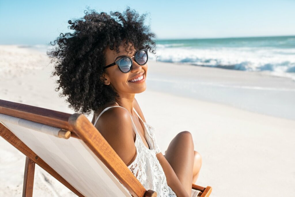 Mulher na praia usando óculos de sol e sorrindo