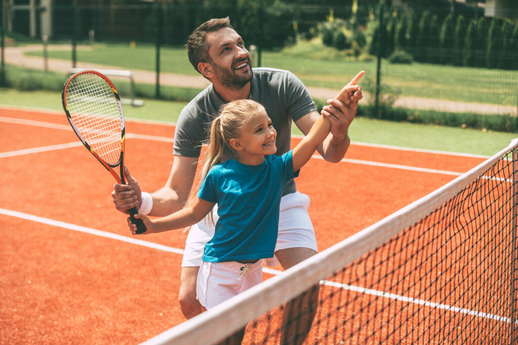 Pai ensinando filha a joga tênis