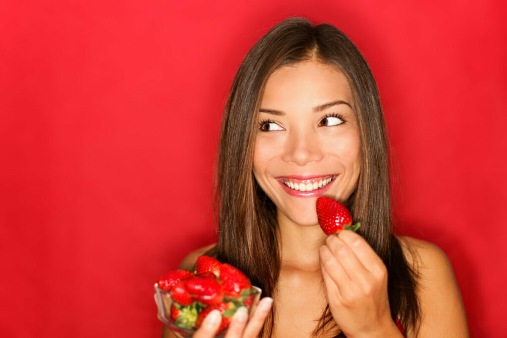 Mulher sorrindo segurando um recipiente com morangos em frente a um fundo vermelho