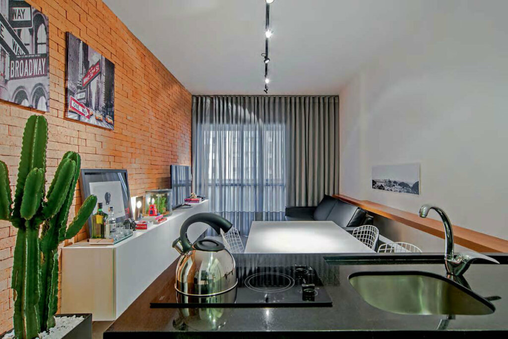 Sala de estar com parede laranja e sofá preto integrada com cozinha