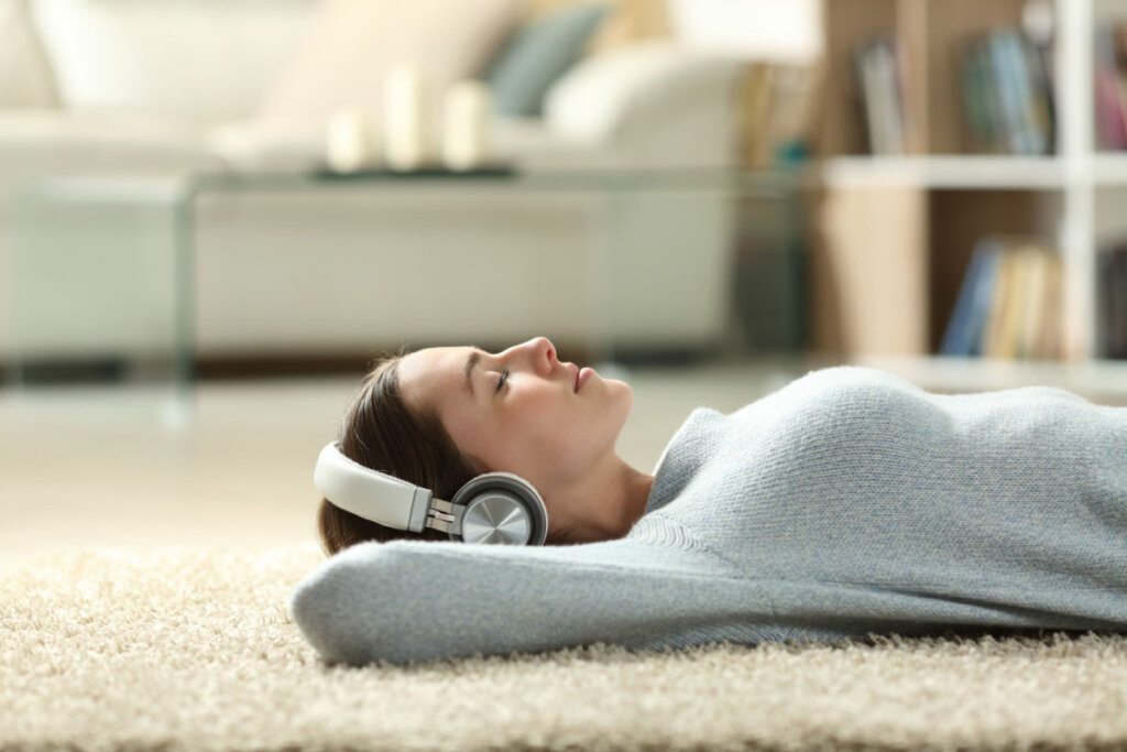 Mulher jovem deitada em um tapete bege e com fones de ouvido.