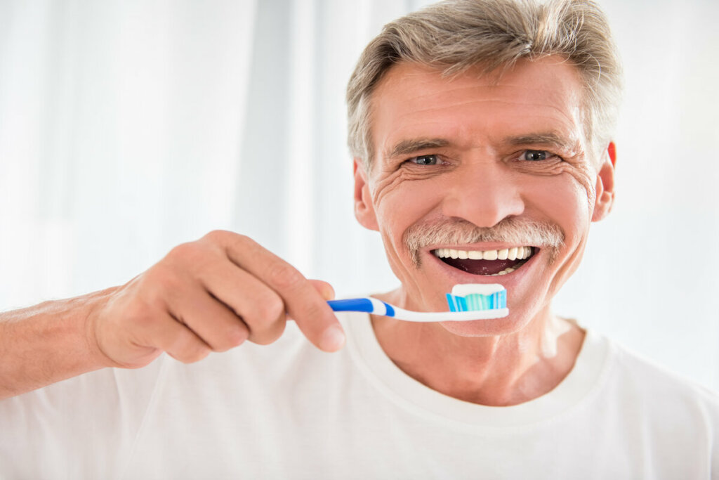 Homem sorrindo segurando uma escova de dente com pasta