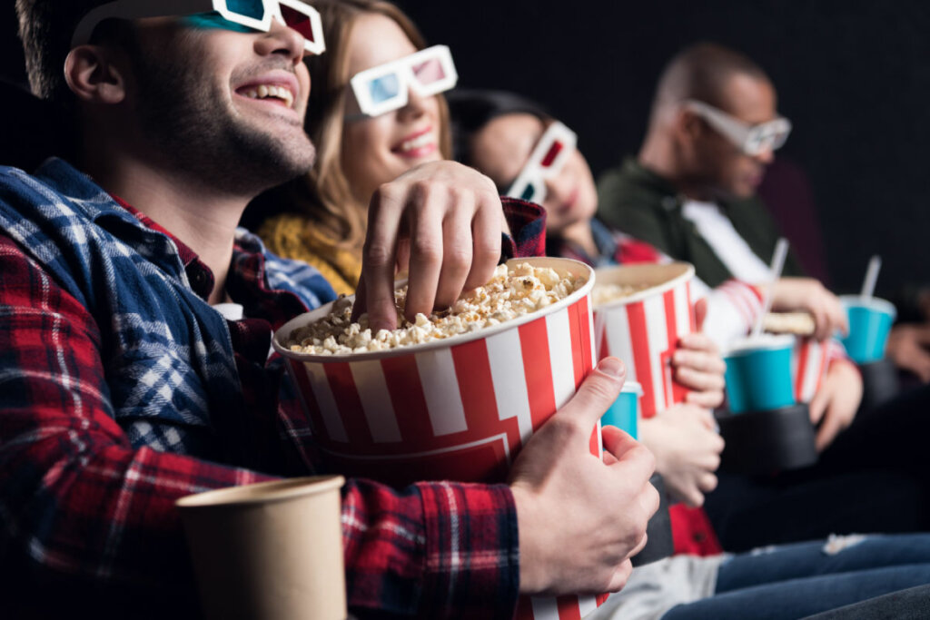 Jovens amigos sorridentes em óculos 3d comendo pipoca e assistindo filme no cinema