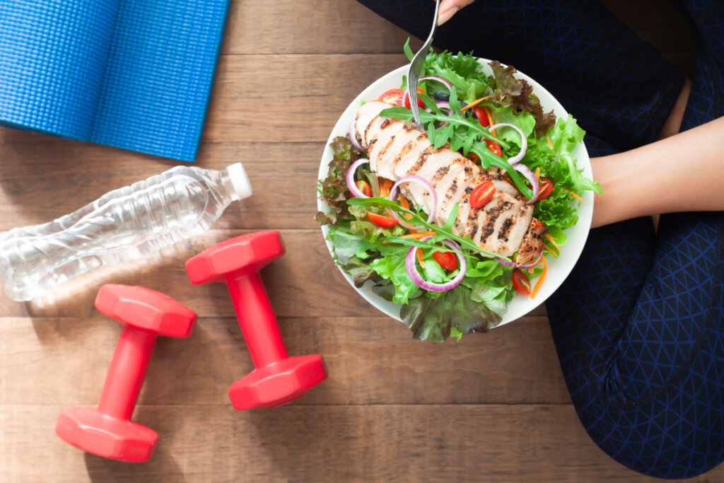 Comida saudável e fitness. Prato de salada de frango com equipamentos de ginástica