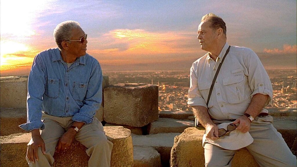 Dois homens sentados em pedras, no pôr do Sol, conversando entre si