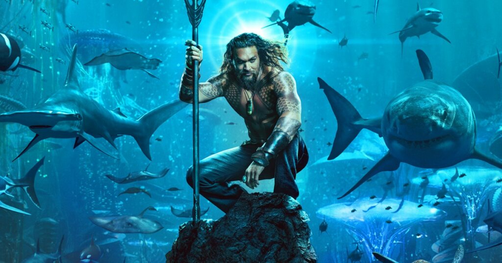 Imagem fictícia mostra super-herói Aquaman rodeado de tubarões embaixo do oceano.