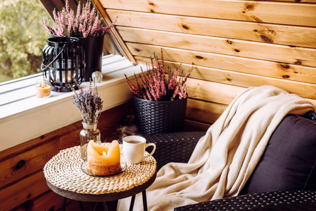 Ambiente com poltrona preta, manta bege, mesa com vela, chá e plantas 