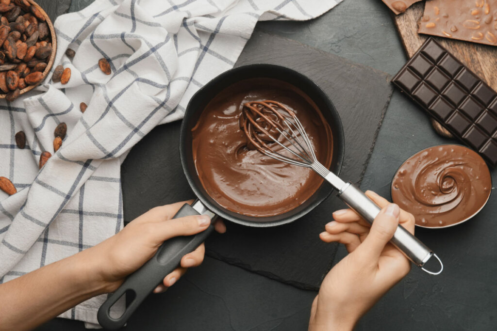 Mãos mexendo chocolate derretido em panela preta