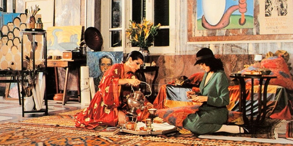 Na imagem, representação de duas artistas do século 20 sentadas em uma tapeçaria bebendo chá. O local é rodeado de obras da Tarsila do Amaral.