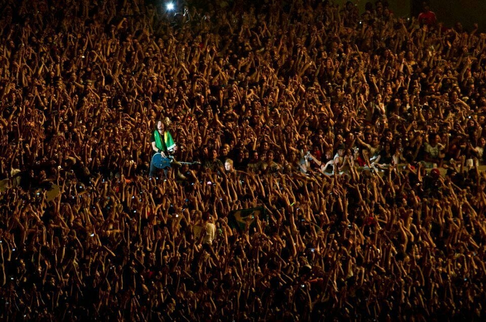 Vocalista Foo Fighters no meio da plateia com bandeira do Brasil nos ombros