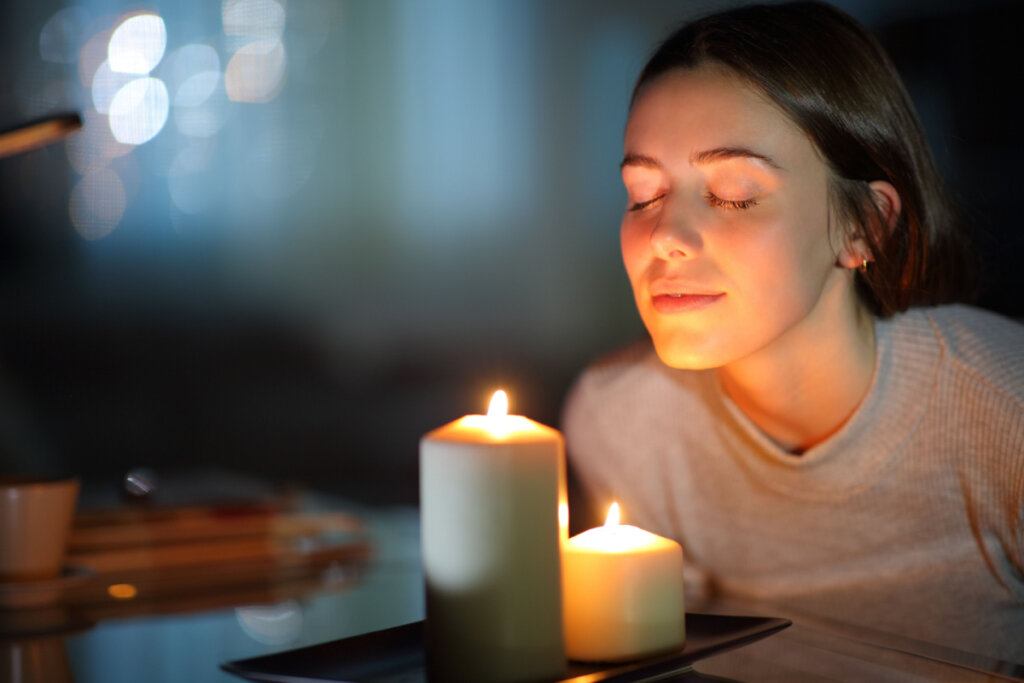 Mulher com expressão relaxada sentindo o aroma de velas acesas durante a noite