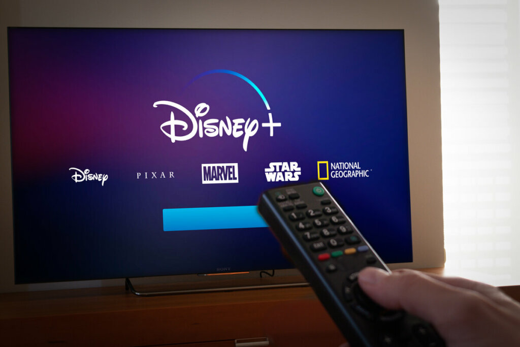 Logo do Disney+ em uma televisão com pessoa segurando um controle remoto