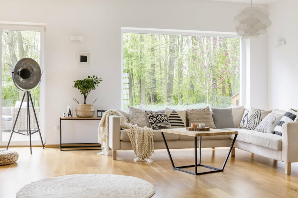 Sala de estar com janela ao fundo, sofá branco e mesa de centro de madeira 